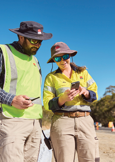 a male and female worker in fluro vest looking at their phone in a construction zone