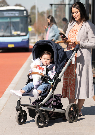 Mother pushing a baby in a pram, standing under a bus stop