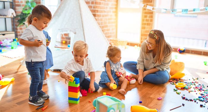 Image of a teacher and group of toddlers playing with lots of toys at childcare