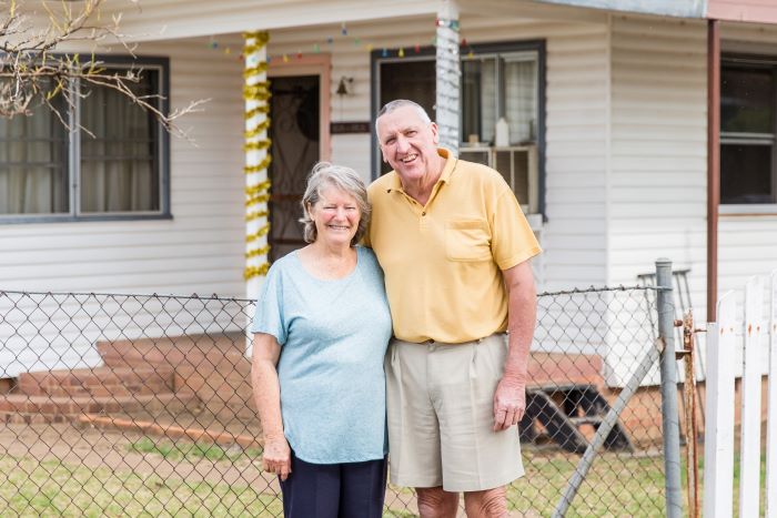 Image of a happy retired husband and wife standing arm in arm in front of their house in Elsmore in the Hunter region