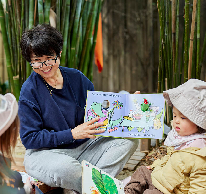 A early childhood educator reading a book in an outside classroom