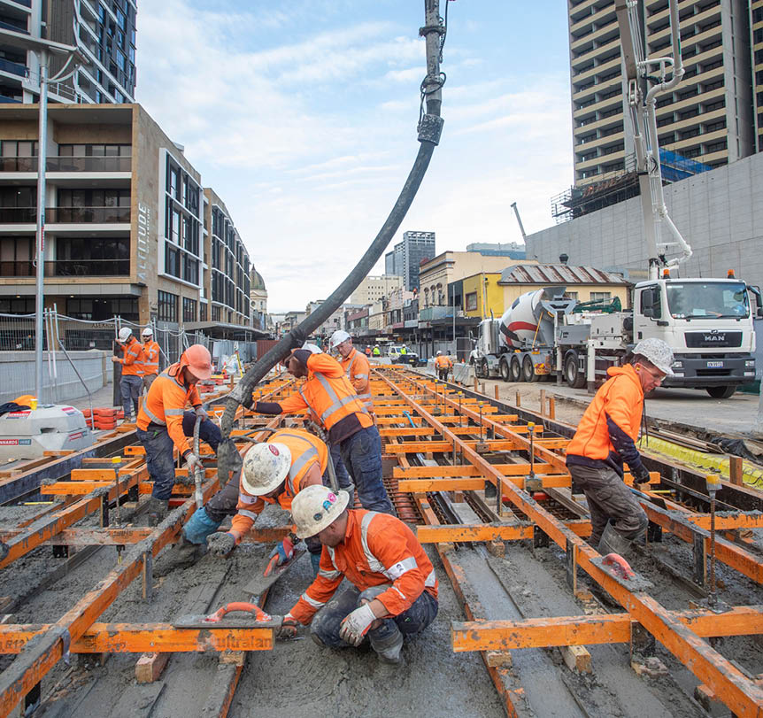 Construction workers pouring concrete into light rail track cast