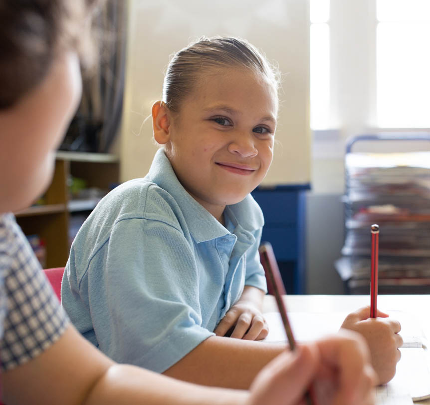 A First Nations child sitting at a desk in a classrom with pencils