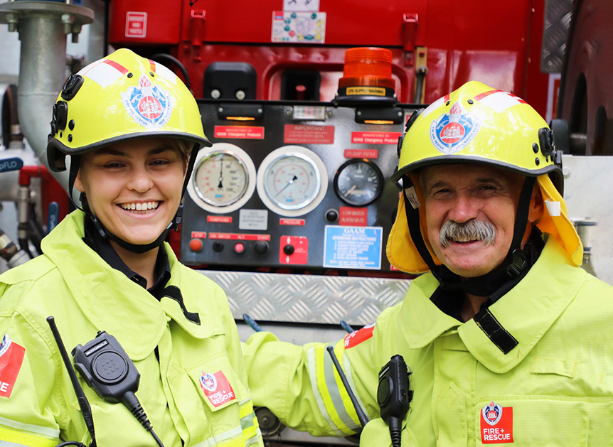 Two firefighters in uniform smiling.