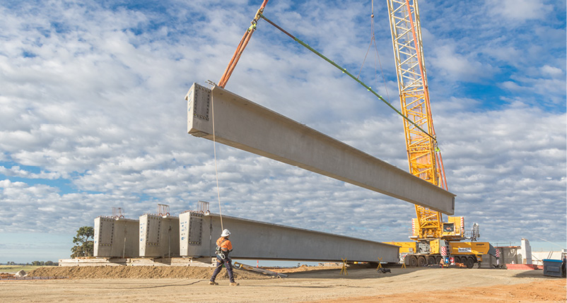 A construction worker with a hard hat and high-vis shirt walking past a crane.
