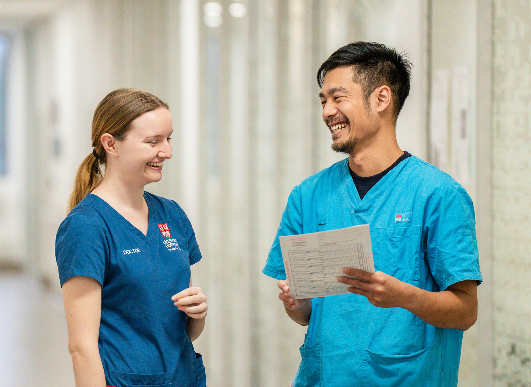 Two healthcare workers in scrubs smiling and talking at a hospital