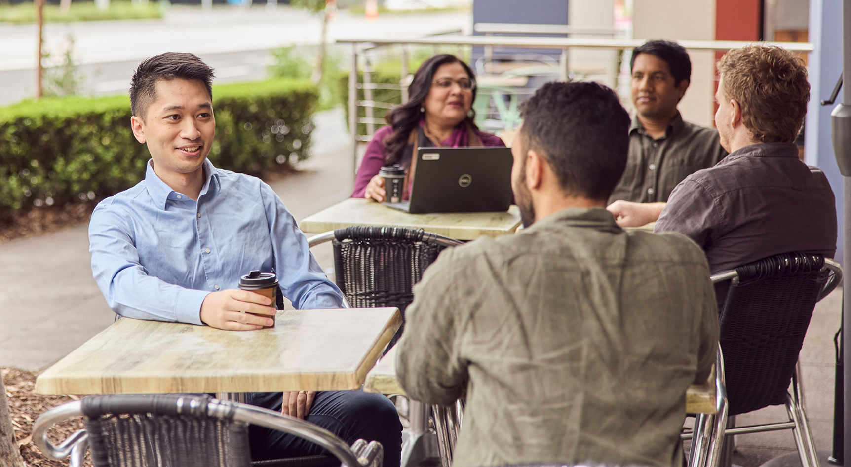 A group of people with takeaway coffee cups sitting at tables outside