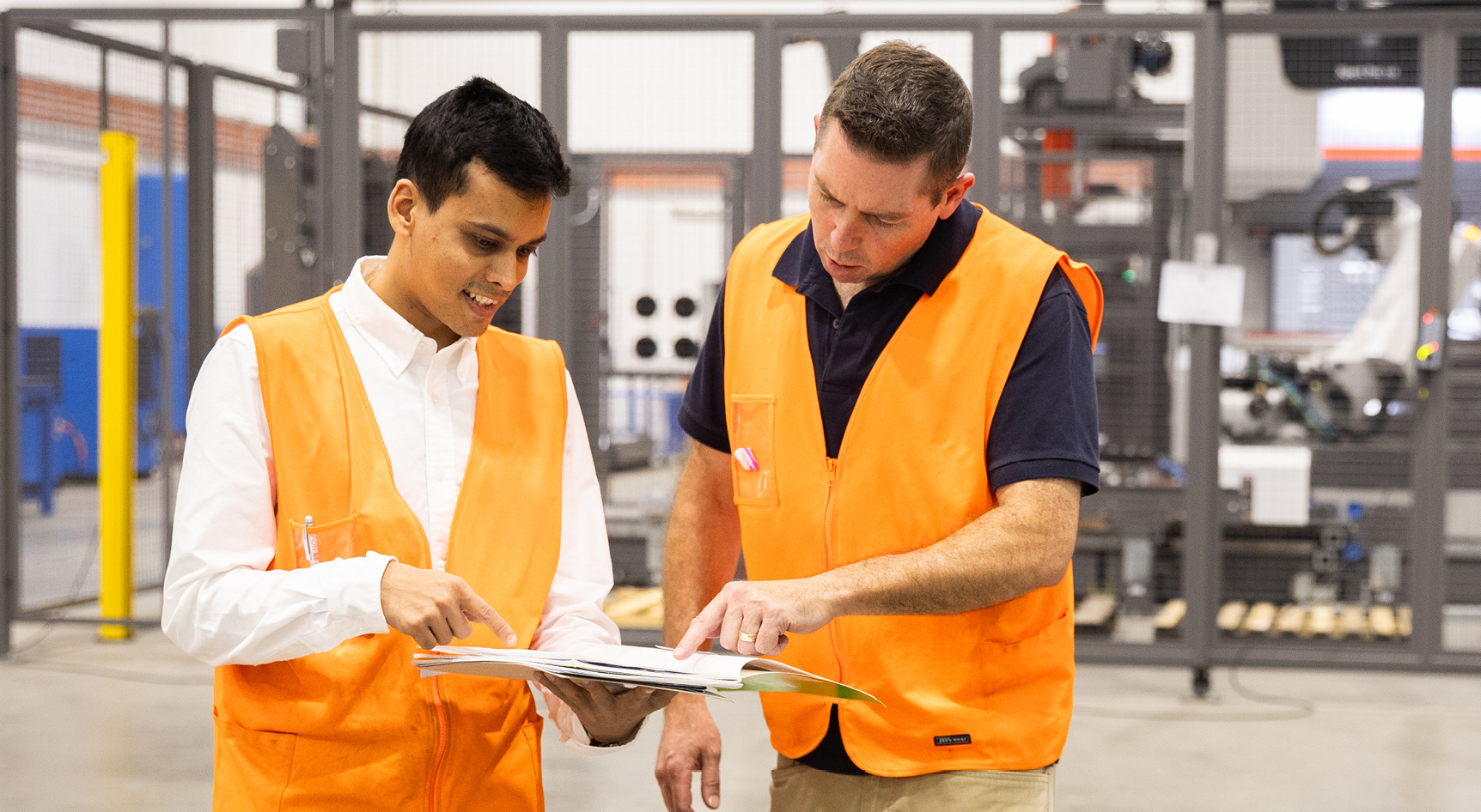 Two people in high-vis vests looking at a piece of paper at a factory