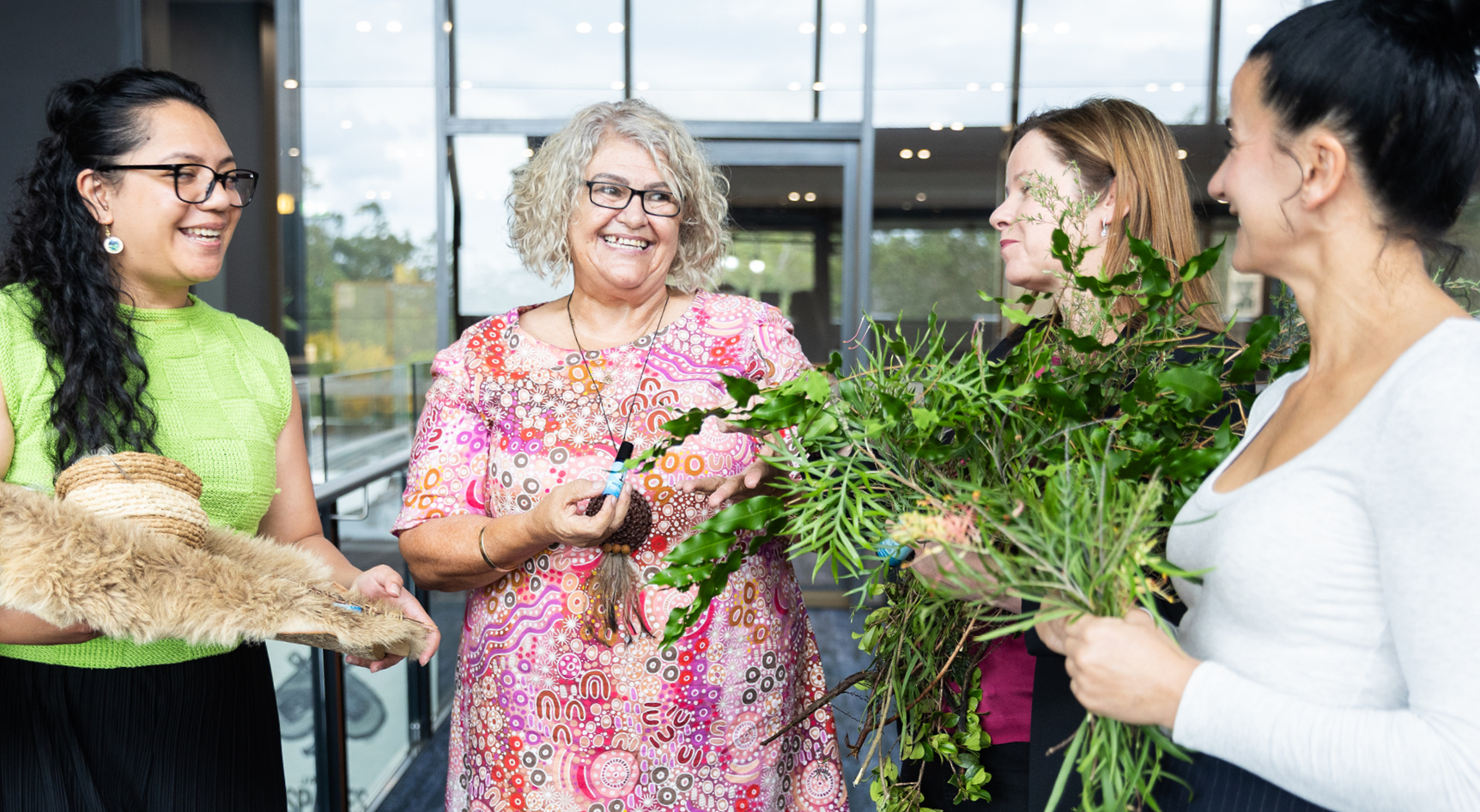 A group of women smiling holding plants and animal skin in a room