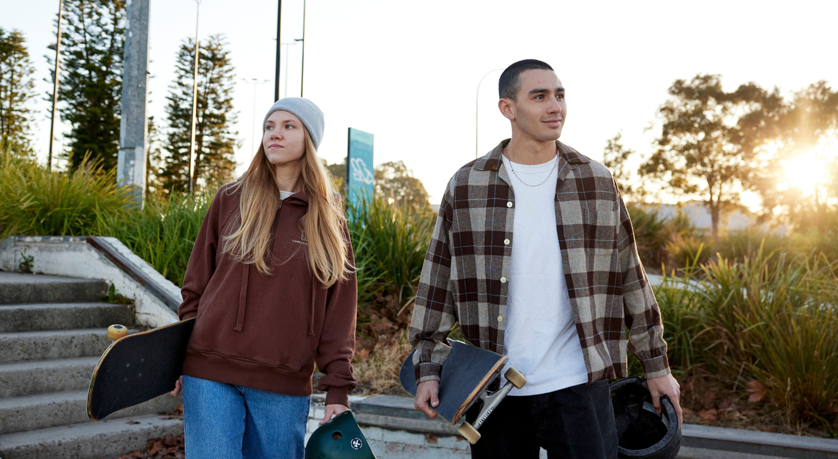 Two people holding skateboards and helmets in a park