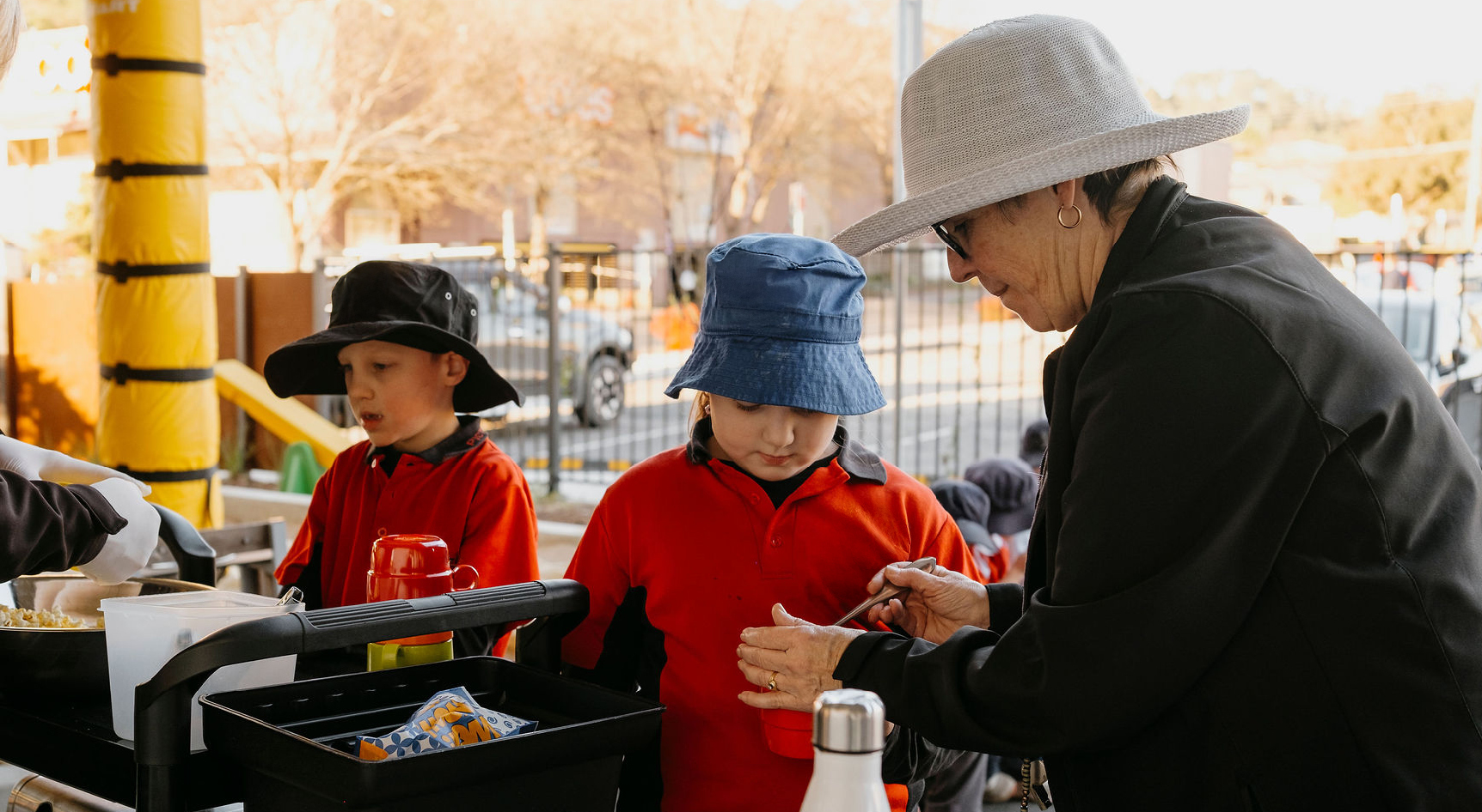 Children in school uniforms being served snacks in the school yard